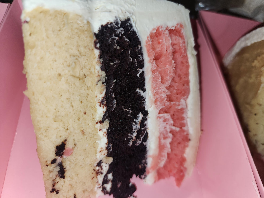 Slice of vegan layer cake with vanilla, chocolate and strawberry layers