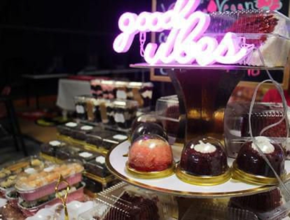 Vintage Vegan dessert display under a Good Vibes neon sign at an event